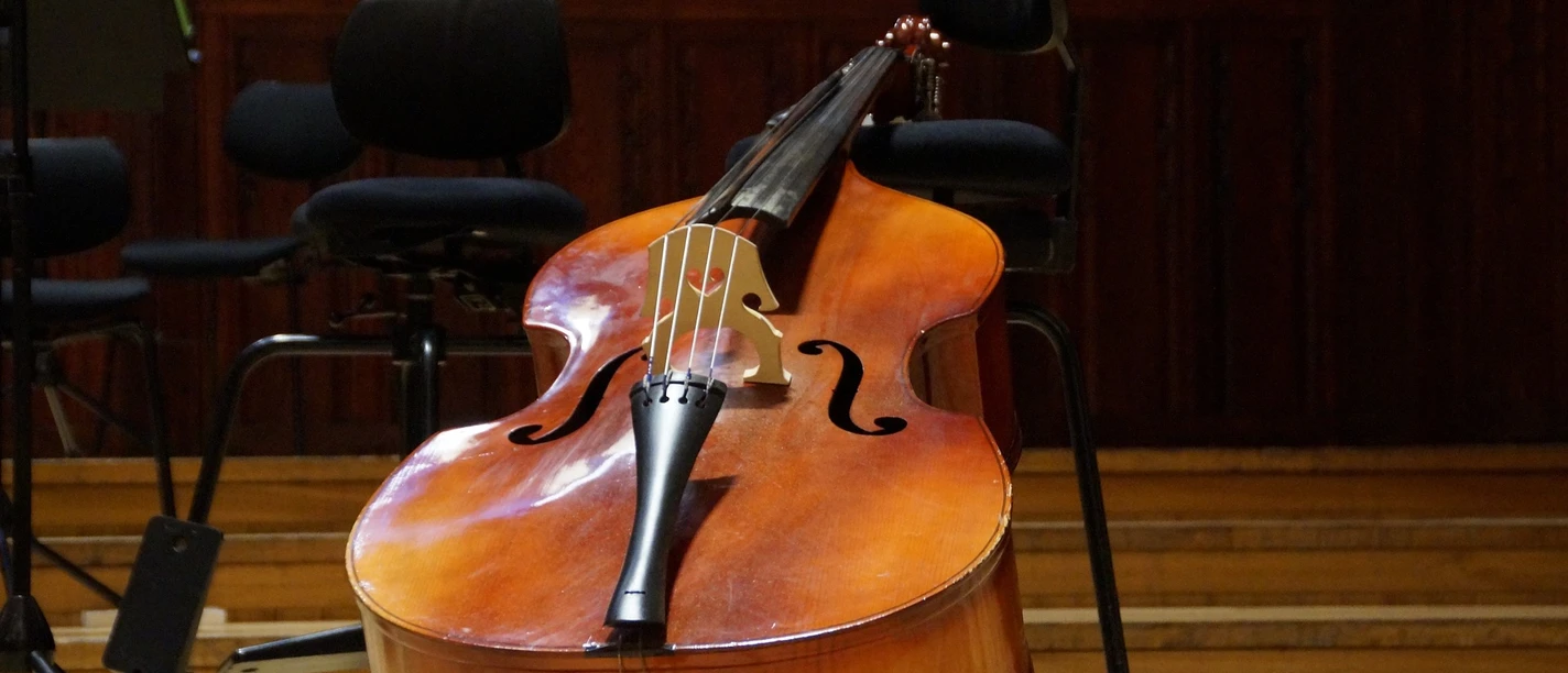 Kontrabass Ein Kontrabass lehnt auf einem hölzernen Konzertboden, umgeben von leeren Musiksesseln.