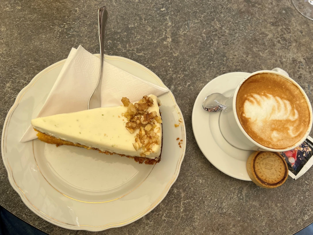 Kaffee_Kuchen Ein Stück Walnusskuchen mit Gabel auf Teller neben einer Tasse Cappuccino auf grauem Steintisch.
