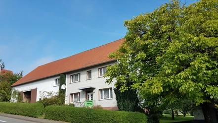 Fassade eines traditionellen Ferienhauses mit rotem Ziegeldach, umgeben von Grünen Büschen und Bäumen.