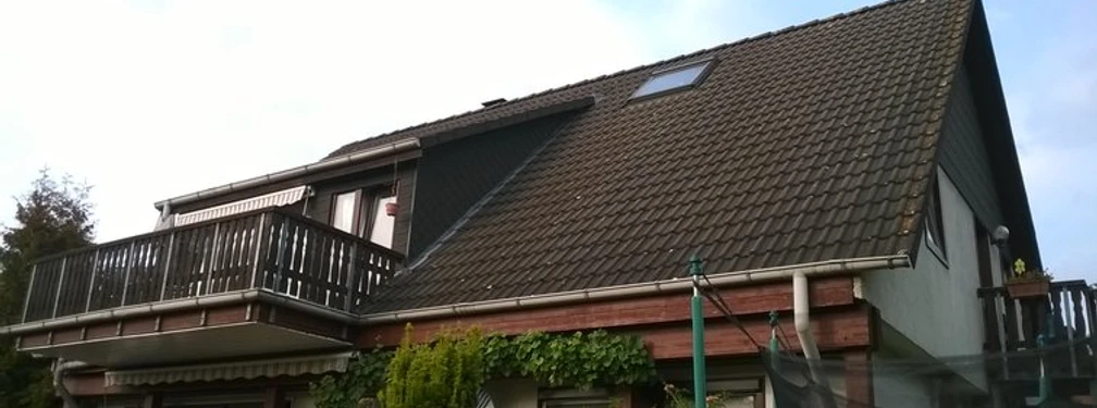Ferienwohnung mit modernem Balkon in einem Gebäude mit steilem Satteldach, umgeben von Natur.