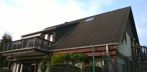 Ferienwohnung Ostmann Ansicht.jpg Ferienwohnung mit modernem Balkon in einem Gebäude mit steilem Satteldach, umgeben von Natur.