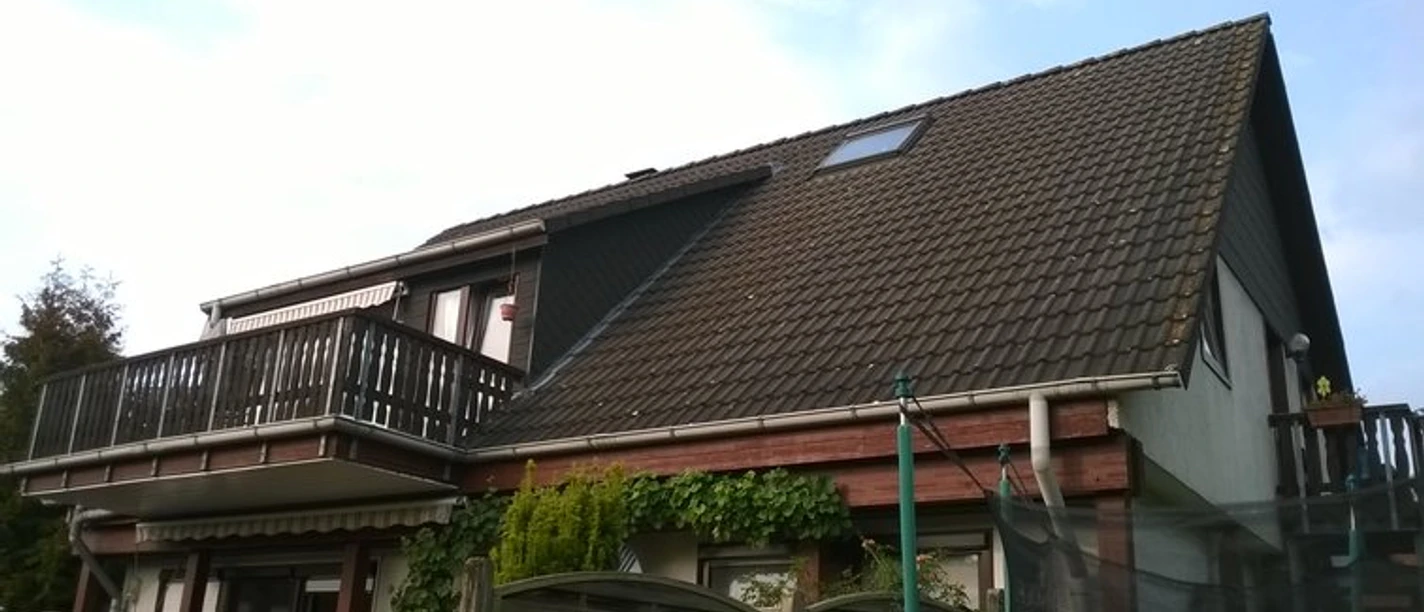 Ferienwohnung Ostmann Ansicht.jpg Ferienwohnung mit modernem Balkon in einem Gebäude mit steilem Satteldach, umgeben von Natur.