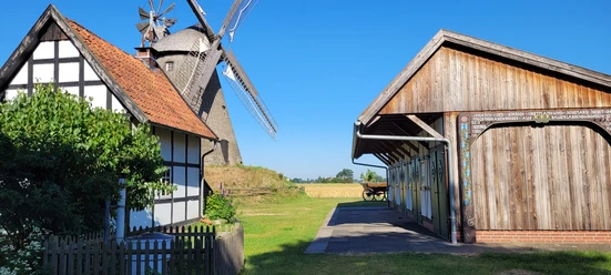 Windmühle Südhemmern Fachwerkhaus und Holzgebäude flankieren die historische Windmühle Südhemmern unter strahlend blauem Himmel.