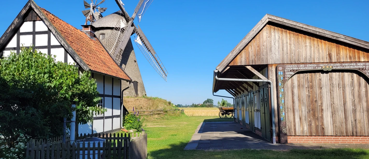 Windmühle Südhemmern Fachwerkhaus und Holzgebäude flankieren die historische Windmühle Südhemmern unter strahlend blauem Himmel.