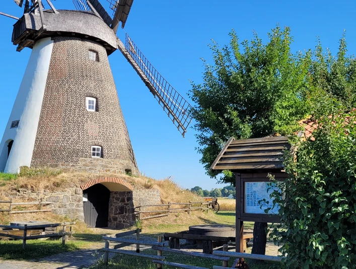 Historische Windmühle Südhemmern, umgeben von grünem Land, blauer Himmel und Rastplatz mit Info-Tafel.