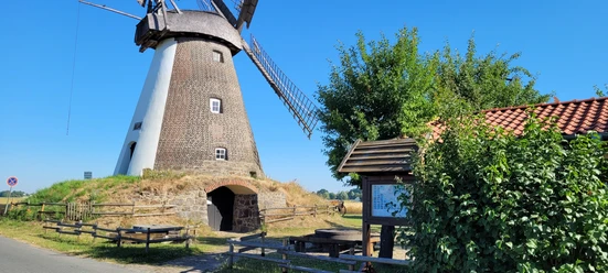 Windmühle Südhemmern Historische Windmühle Südhemmern, umgeben von grünem Land, blauer Himmel und Rastplatz mit Info-Tafel.