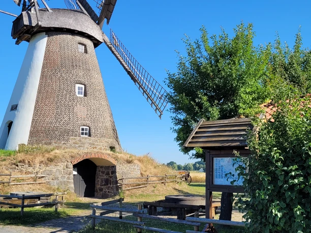 Windmühle Südhemmern Historische Windmühle Südhemmern, umgeben von grünem Land, blauer Himmel und Rastplatz mit Info-Tafel.