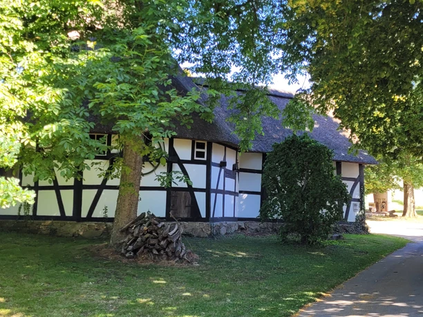 Rossmühle Oberbauerschaft Ein historisches Fachwerkgebäude mit Reetdach, umgeben von Schatten spendenden Bäumen und gepflegtem Rasen.