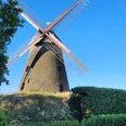 Historische Windmühle Nordhemmern mit großen Flügeln, umgeben von grünen Bäumen und Hecken.