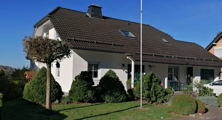 Ein modernes Einfamilienhaus mit braunem Satteldach, umgeben von gepflegtem Garten und blauen Himmel.