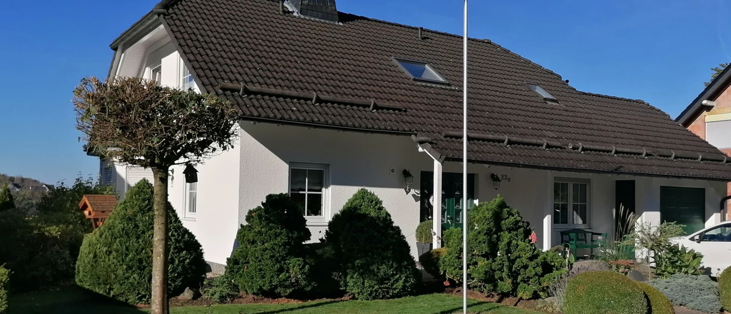Ein modernes Einfamilienhaus mit braunem Satteldach, umgeben von gepflegtem Garten und blauen Himmel.