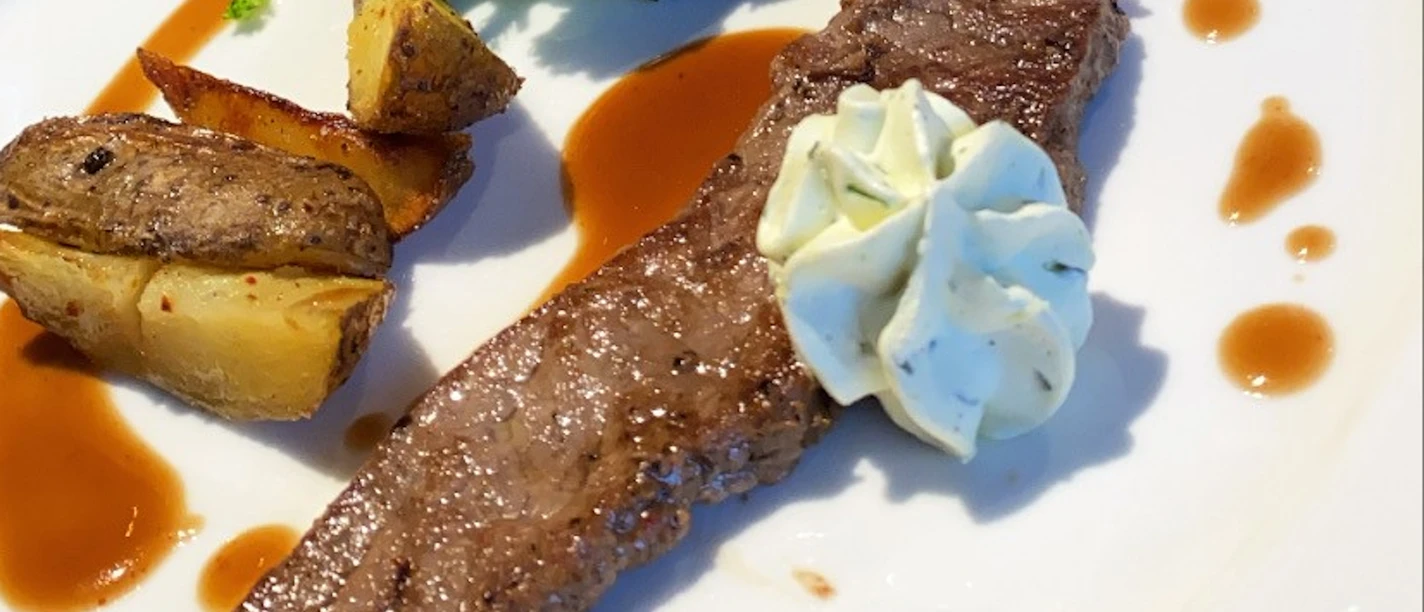 Fleischgericht Saftiges Steak mit Kartoffelspalten, Brokkoli und einer feinen Kräuterbutter auf elegantem Teller.