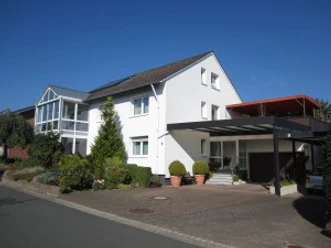 Ferienwohnung Brigitte u. Wolfgang Waldow.jpg Zweistöckiges Haus mit weißer Fassade, darüber ein blauer Himmel; links Wintergarten.