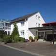 Ferienwohnung Brigitte u. Wolfgang Waldow.jpg Zweistöckiges Haus mit weißer Fassade, darüber ein blauer Himmel; links Wintergarten.