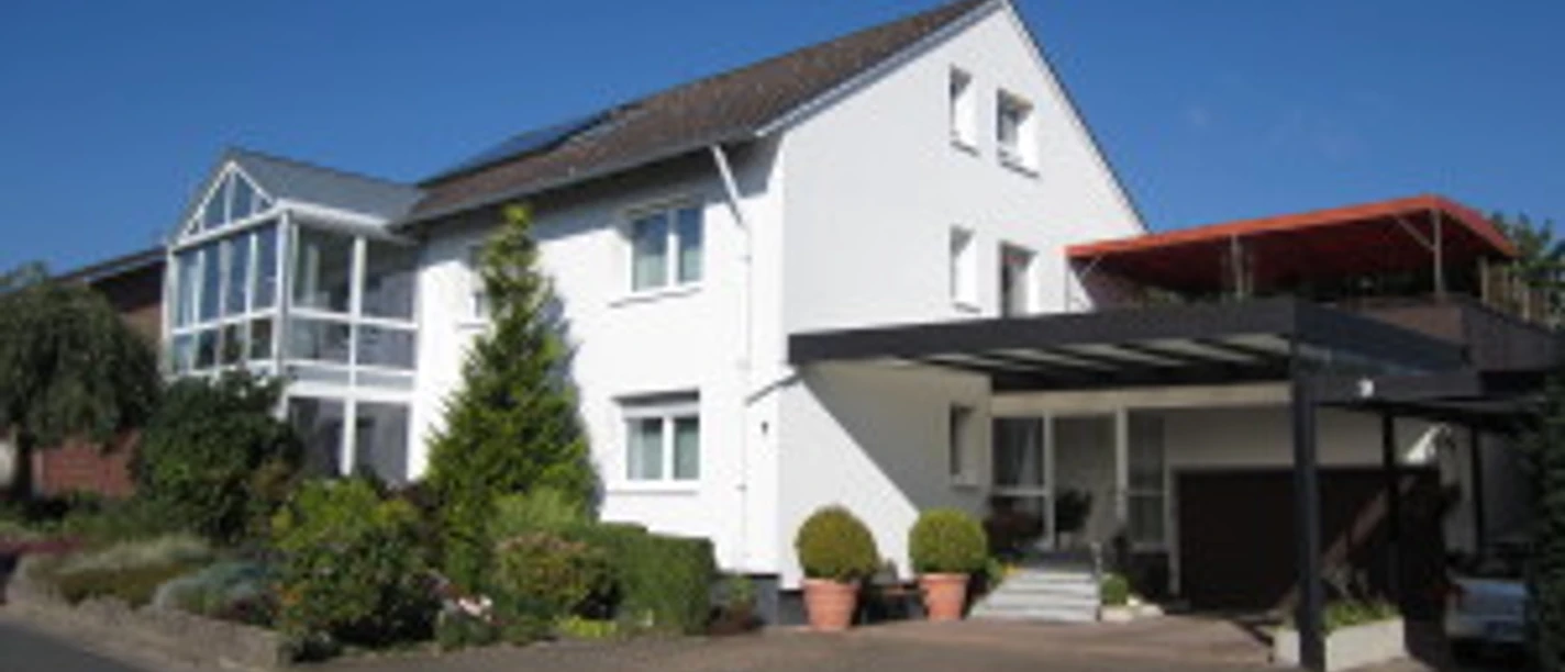 Ferienwohnung Brigitte u. Wolfgang Waldow.jpg Zweistöckiges Haus mit weißer Fassade, darüber ein blauer Himmel; links Wintergarten.