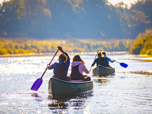 Kanu CR MedienAtelier Emsland.jpg Menschen paddeln in Kanus auf der Ems, Sonnenlicht spiegelt im Wasser, umgeben von grüner Landschaft.