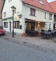 Louis Prima.jpg Pizzeria mit Außenterrasse und roten Dachziegeln in ruhiger Seitenstraße, Laterne und Auto daneben.