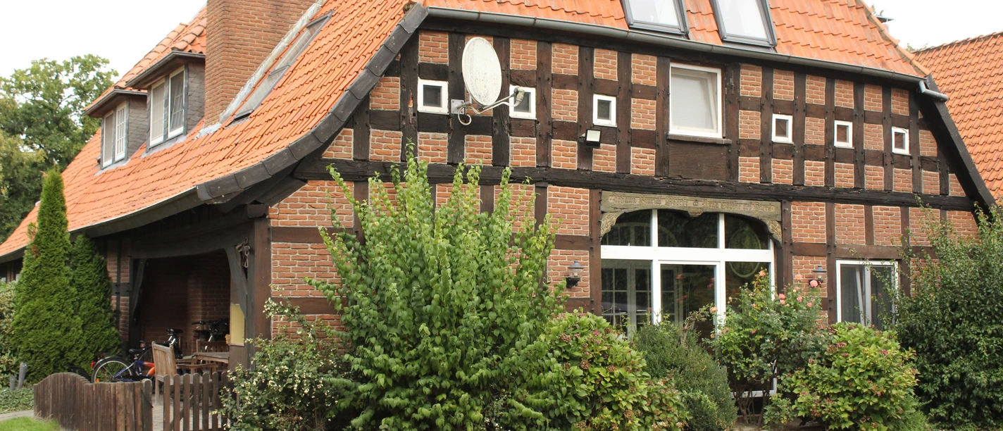 Half-timbered house with red roof tiles and large windows, surrounded by lush vegetation and shrubs.