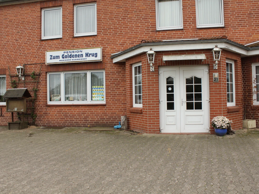 Zum Goldenen Krug Backsteingebäude mit weißen Türen und Fenstern, über denen ein Schild "Pension Zum Goldenen Krug" prangt.