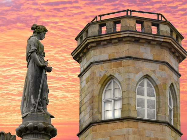 (c) Werner Wilmes-RathausturmundStatue.jpg Steinerne Statue neben farblich belebtem Rathausturm vor einem dramatischen Sonnenuntergangshimmel.