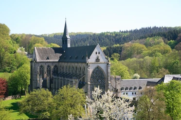 Altenberger Dom Eine gotische Abtei inmitten grüner Wälder und blühender Bäume unter klarem, blauem Himmel.