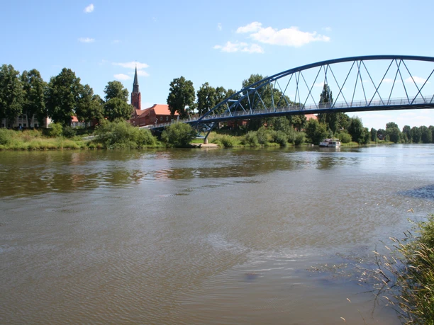 Eine blaue Stahlbrücke erstreckt sich über die breiten Weser, umgeben von grüner Ufervegetation.