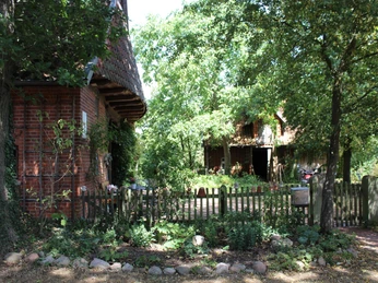 Dat Lüttke Hues, Petershagen Backsteinhaus mit Reetdach, Holzoberstock, umgeben von Bäumen und einem Zaun, an einem sonnigen Tag.