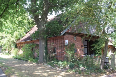 Dat Lüttke Hues, Petershagen Historisches Fachwerkhaus mit roten Ziegelsteinen und blühendem Garten, umgeben von alten Bäumen.
