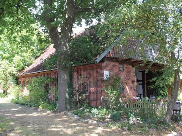 Dat Lüttke Hues, Petershagen Historisches Fachwerkhaus mit roten Ziegelsteinen und blühendem Garten, umgeben von alten Bäumen.