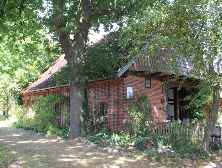 Dat Lüttke Hues, Petershagen Historisches Fachwerkhaus mit roten Ziegelsteinen und blühendem Garten, umgeben von alten Bäumen.
