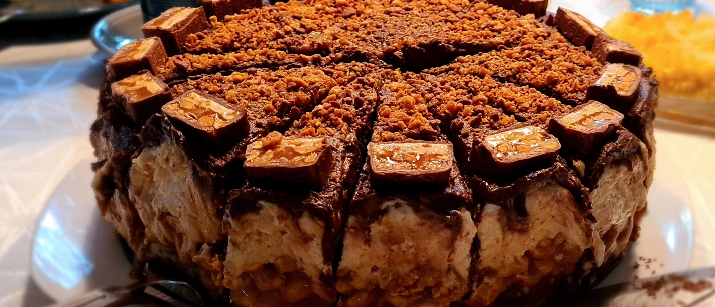 Eine reichhaltige Schokoladentorte mit Karamellstücken oben und cremigen Schichten darunter.