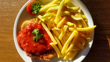 Schnitzel mit Pommes_CCBYSA_Teutoburger Wald_Stadt Schloss Holte-Stukenbrock-33.jpg Schnitzel mit roter Soße und grüner Garnitur, serviert mit knusprigen Pommes auf weißem Teller.