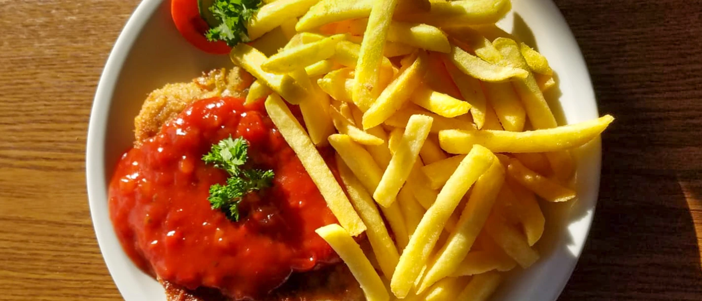 Schnitzel mit Pommes_CCBYSA_Teutoburger Wald_Stadt Schloss Holte-Stukenbrock-33.jpg Schnitzel mit roter Soße und grüner Garnitur, serviert mit knusprigen Pommes auf weißem Teller.