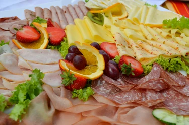 Vielfältige Frühstücksplatte mit Aufschnitt, Käse, frischen Erdbeeren, Orangenscheiben und Trauben.