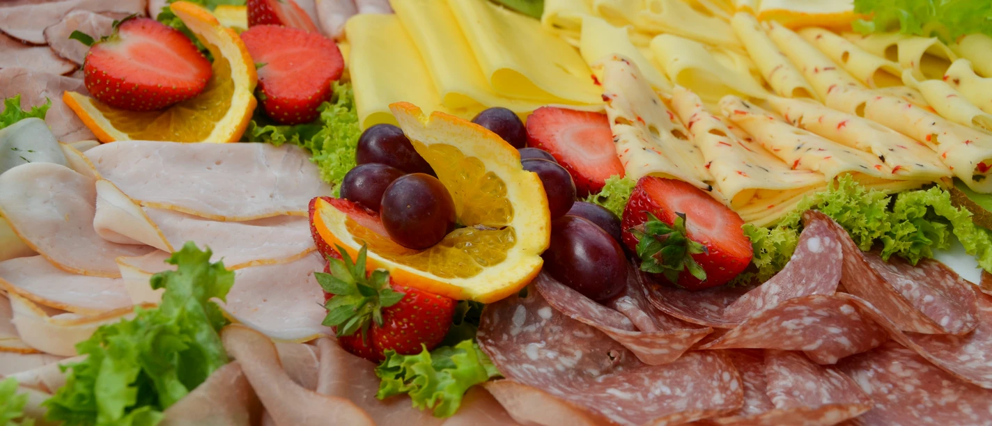 Vielfältige Frühstücksplatte mit Aufschnitt, Käse, frischen Erdbeeren, Orangenscheiben und Trauben.
