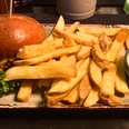 Ein Cheeseburger mit grünen Salatblättern, serviert mit dicken Pommes und weißem Dip auf brauner Platte.