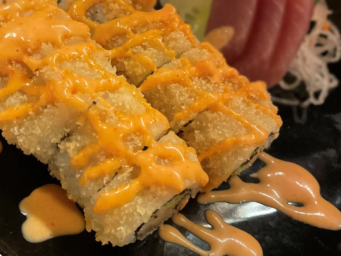 Sushi-Tempura-Gericht auf schwarzem Teller mit knusprigem Teig und würziger Soße garniert.