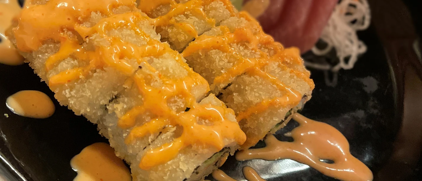 Sushi-Tempura-Gericht auf schwarzem Teller mit knusprigem Teig und würziger Soße garniert.