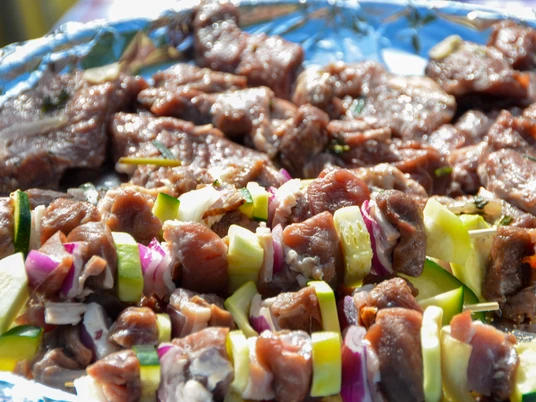 Grillgut_SHS_CC-BY-SA_Teutoburger_Wald_Stadt_Schloss_Holte-Stukenbrock.jpg Nahaufnahme von mariniertem Fleisch und buntem Gemüse auf Spießen, bereit zum Grillen.