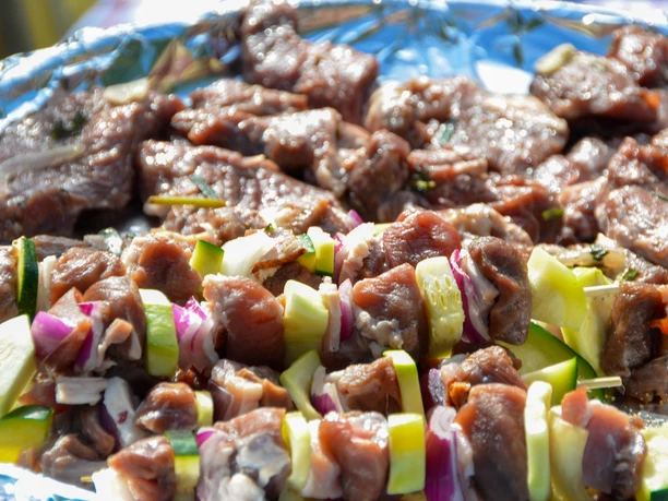 Grillgut_SHS_CC-BY-SA_Teutoburger_Wald_Stadt_Schloss_Holte-Stukenbrock.jpg Nahaufnahme von mariniertem Fleisch und buntem Gemüse auf Spießen, bereit zum Grillen.