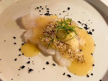 Fischfilet mit heller Sauce, gehackten Nüssen und Kräutern elegant auf weißem Teller angerichtet.