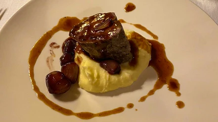 Ein Teller mit Kartoffelpüree, darauf ein Stück Fleisch und Zwiebeln in Bratensoße angerichtet.