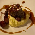 Ein Teller mit Kartoffelpüree, darauf ein Stück Fleisch und Zwiebeln in Bratensoße angerichtet.