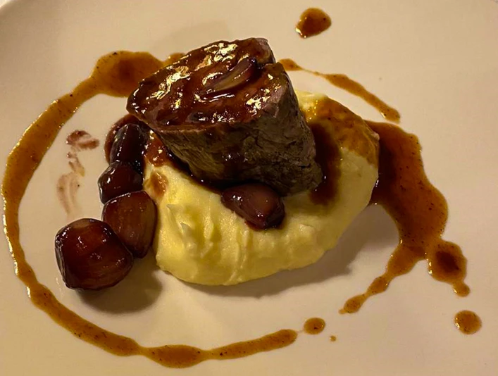 Ein Teller mit Kartoffelpüree, darauf ein Stück Fleisch und Zwiebeln in Bratensoße angerichtet.