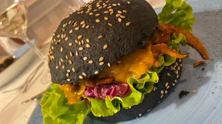 Schwarzer Burger mit Sesam, gefüllt mit Salat, rotem Kraut, Käse und gegrilltem Hähnchen auf Teller.