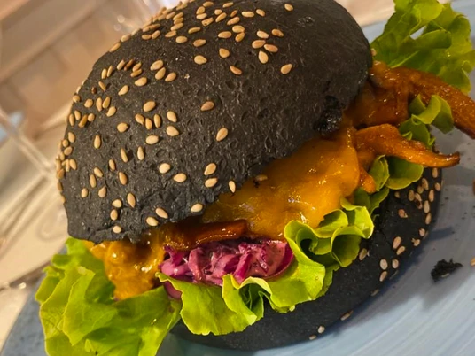 Burger schwarz_CCBYSA_Teutoburger Wald_Stadt Schloss Holte-Stukenbrock-13.jpg Schwarzer Burger mit Sesam, gefüllt mit Salat, rotem Kraut, Käse und gegrilltem Hähnchen auf Teller.