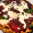 Eine Steinofenpizza mit Bresaola, Rucola, Büffelmozzarella und Parmesanschnipseln auf einem Teller.