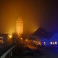 St. Michael im Abendnebel: Beleuchteter Kirchturm ragt aus nebelverschleiertem Ortskern hervor.