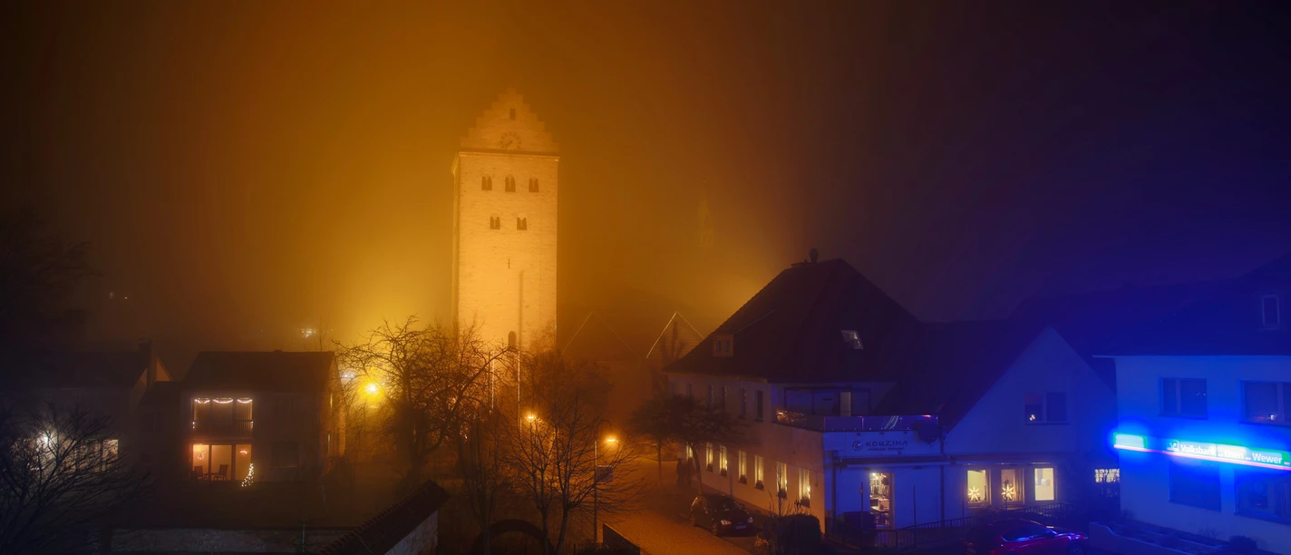 stmichealnebel.jpg St. Michael im Abendnebel: Beleuchteter Kirchturm ragt aus nebelverschleiertem Ortskern hervor.