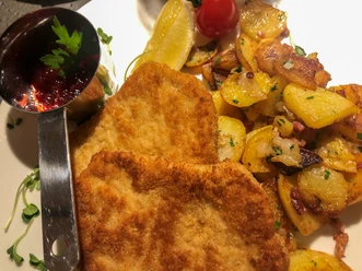 Zwei goldbraun panierte Wiener Schnitzel mit Zitronenscheibe, Preiselbeersoße und Bratkartoffeln.